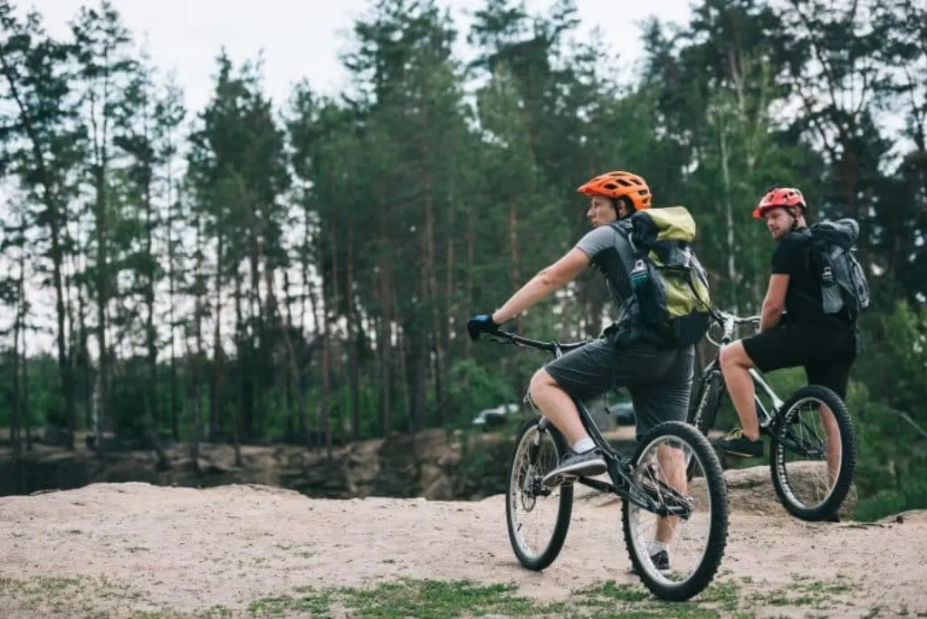 young trial bikers riding in forest on cloudy day